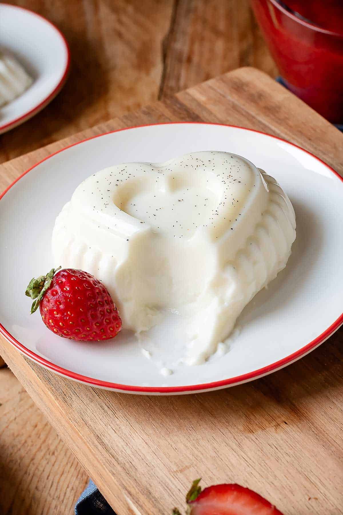 Panna cotta on a dessert plate with a strawberry on the side.