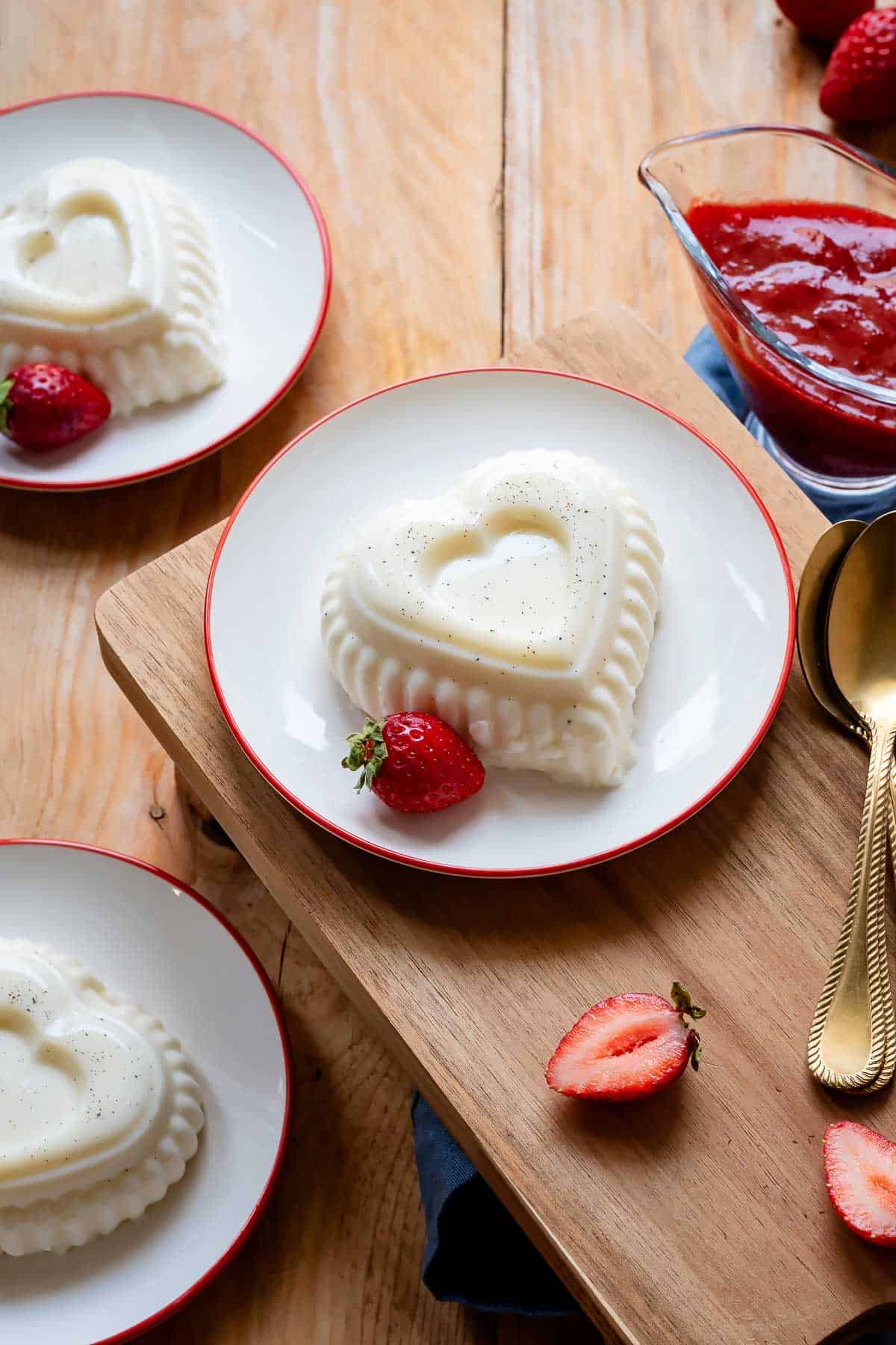 Panna cotta on a dessert plate with red rim and strawberry sauce in the background.