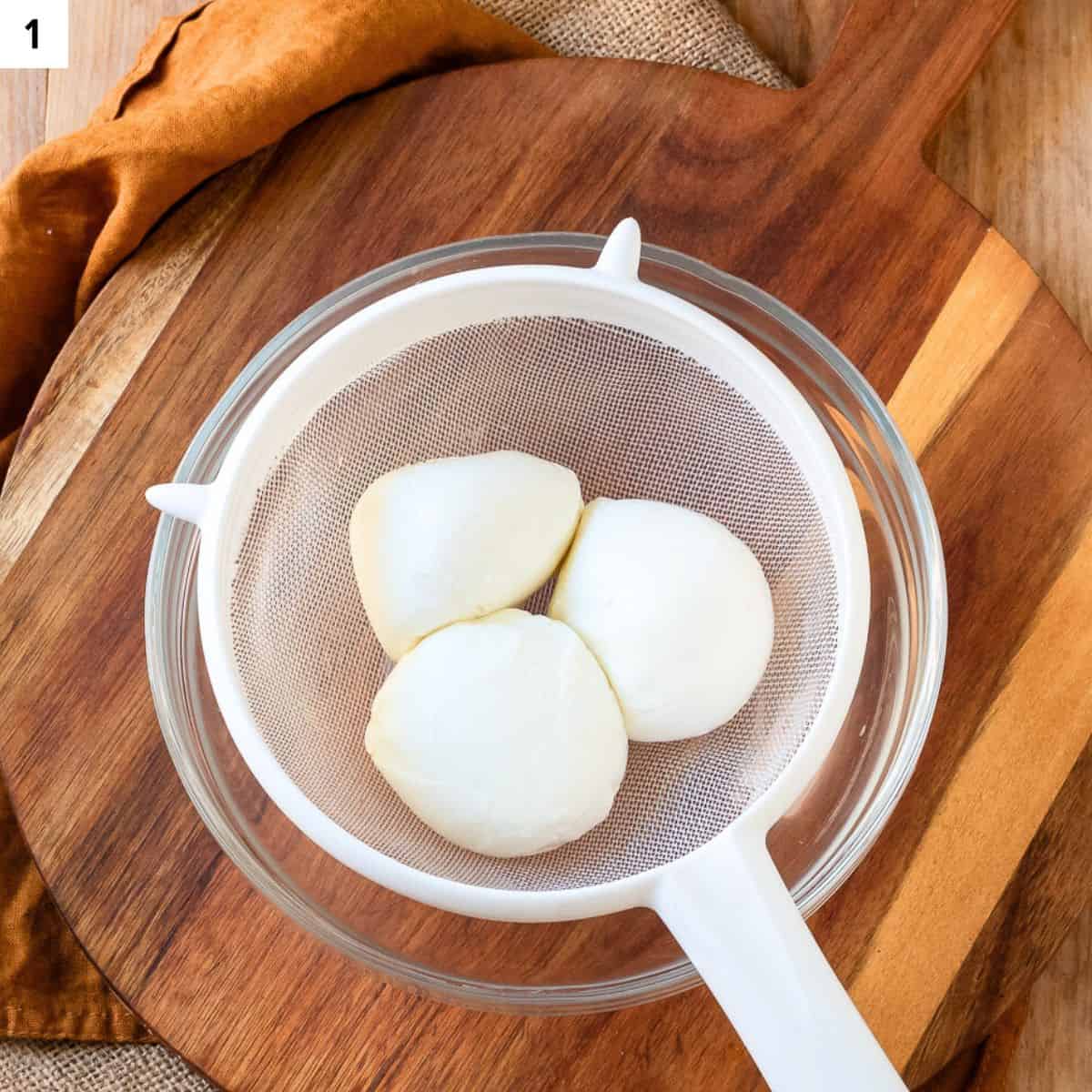 Draining fresh mozzarella from excess liquid over a sieve.