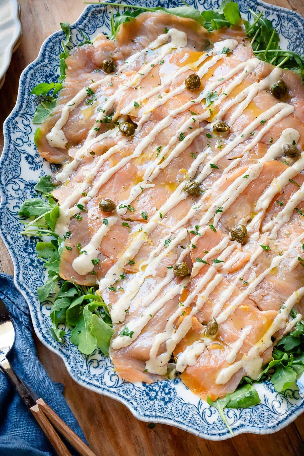 Salmon carpaccio on a serving plate topped with the sauce and garnished with capers and parsley.