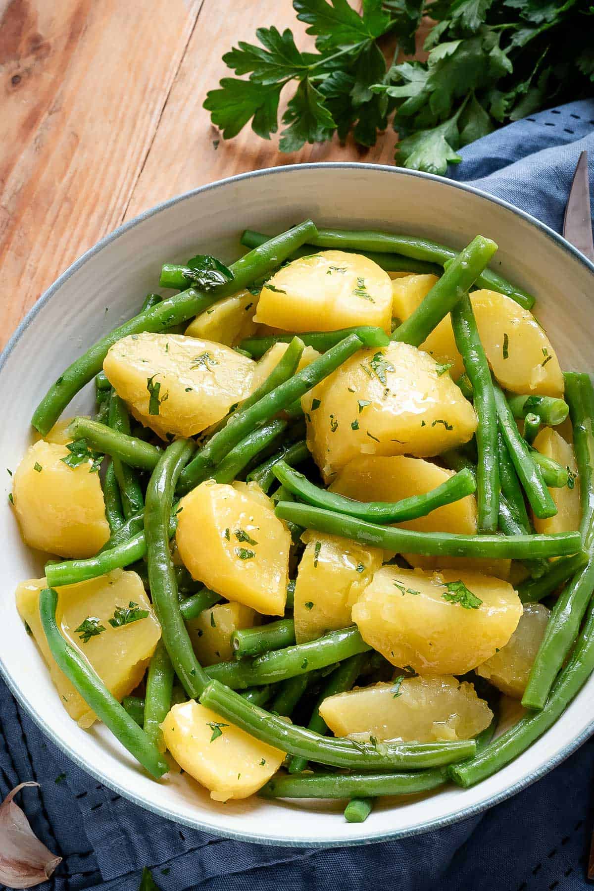 Green beans and potatoes in a white bowl topped with dressing.