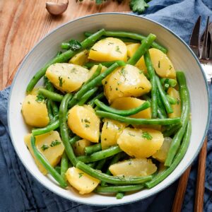 Green beans and potatoes in a white serving bowl with a blue rim.