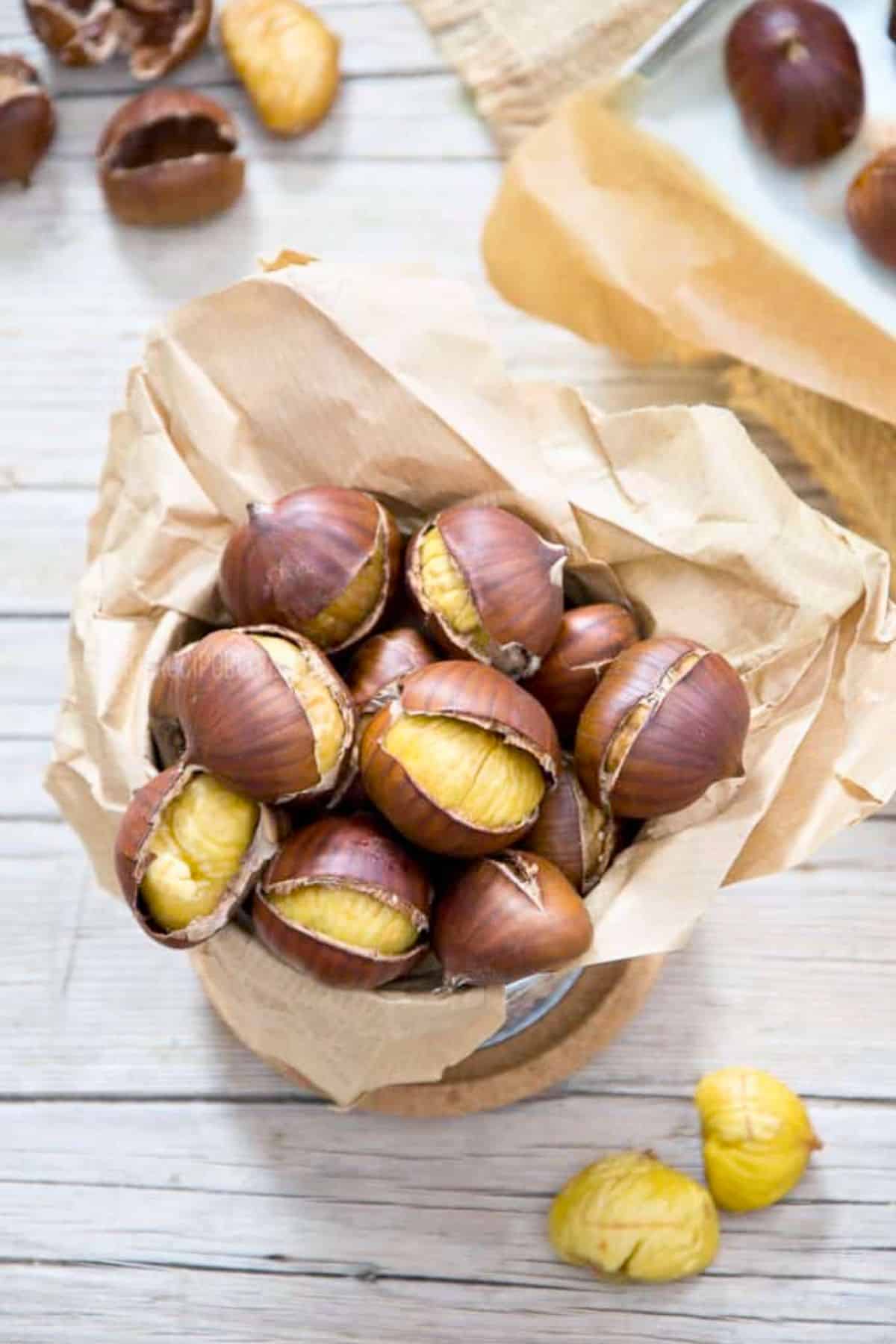 Roasted Chestnuts in a paper cone with peeled chestnuts in the background.