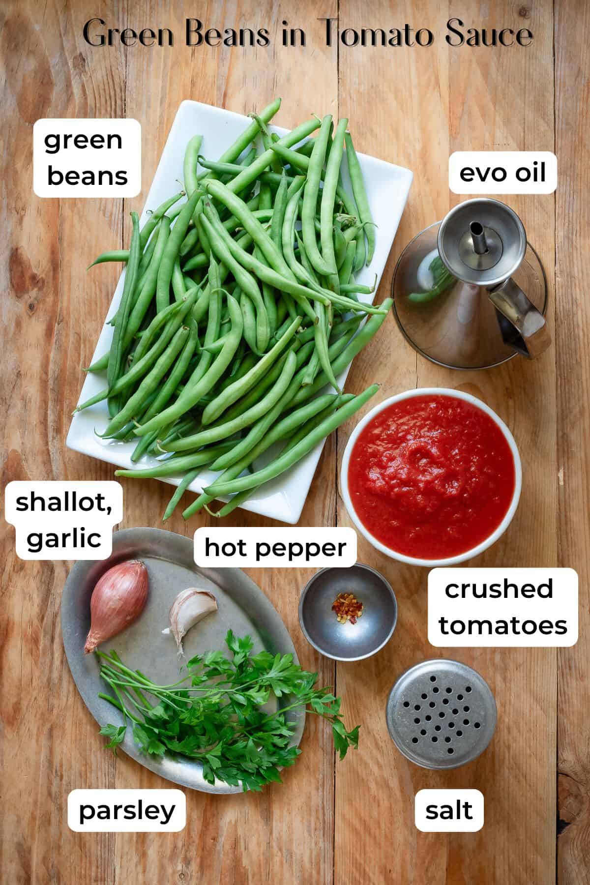 Ingedients needed to make green beans in tomato sauce laid on a wooden surface.