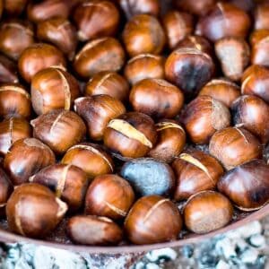 Chestnuts in a pan roasted on open fire with ashes in the background.