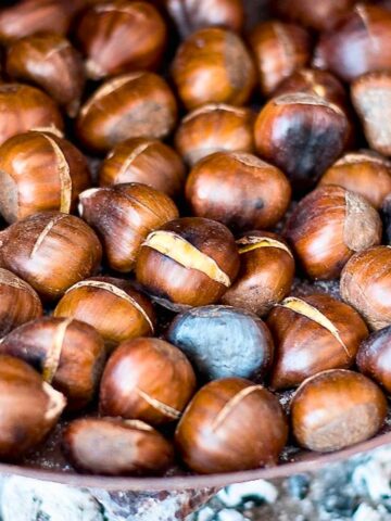 Chestnuts in a pan roasted on open fire with ashes in the background.