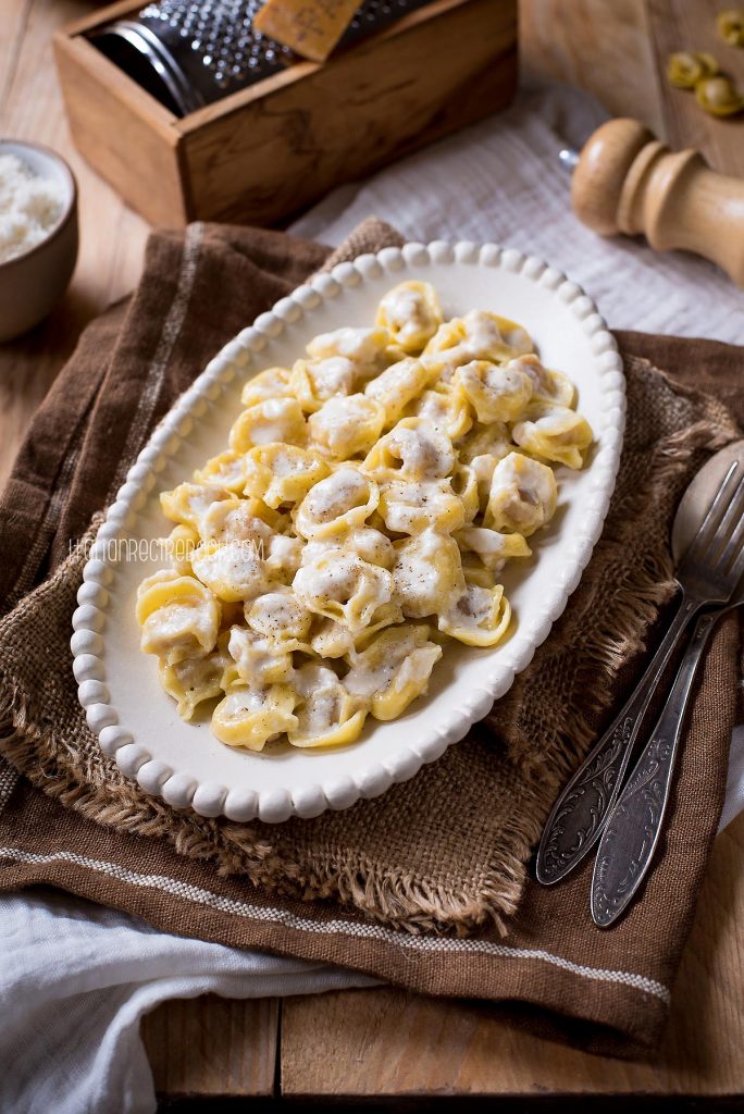 Tortellini alla panna on a plate with pepper shaker and cheese grater in the background.