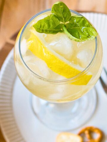 Limoncello spritz cocktail in a glass garnished with a slice of lemon and basil.