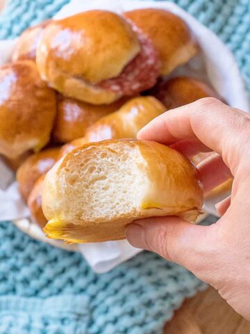 Milk bread roll in hand with more milk rolls in the background.