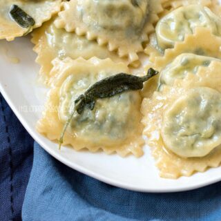 Spinach and ricotta ravioli in sage butter sauce on a plate.