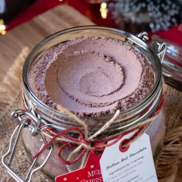 Homemade hot chocolate mix in a glass jar with Christmas decorations in the background.