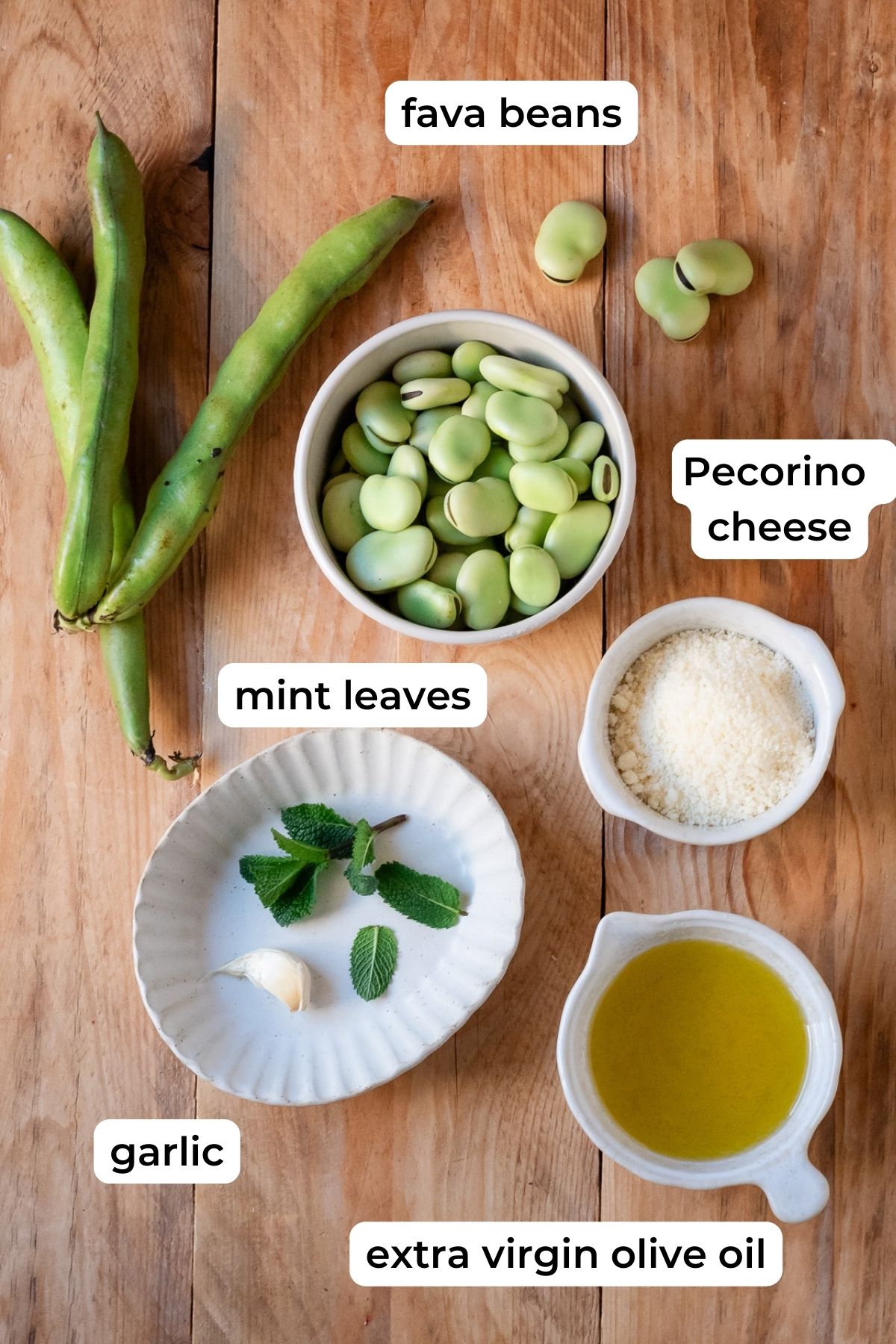 Ingredients needed for fava bean pesto laid on a wooden surface.
