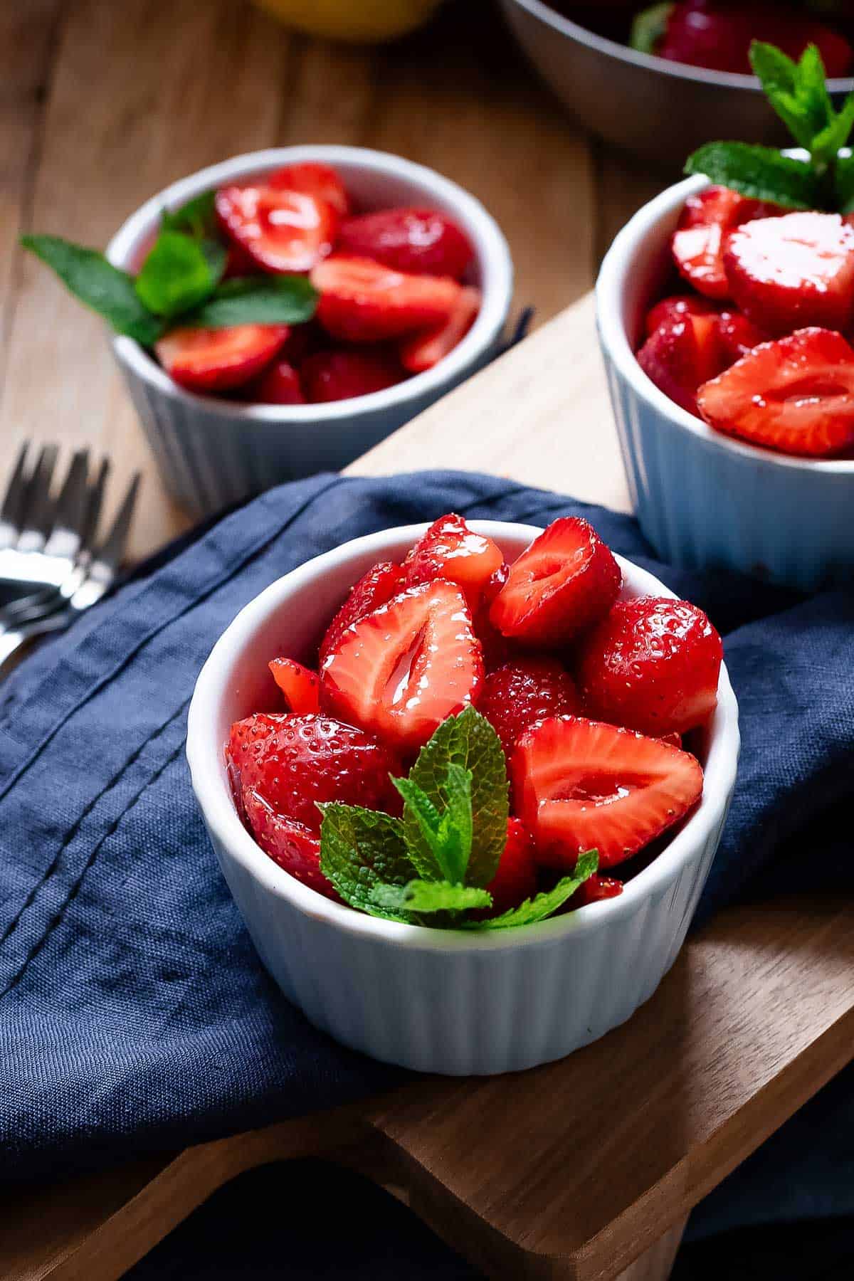 Macerated strawberries in blue serving bowls garnished with mint leaves.