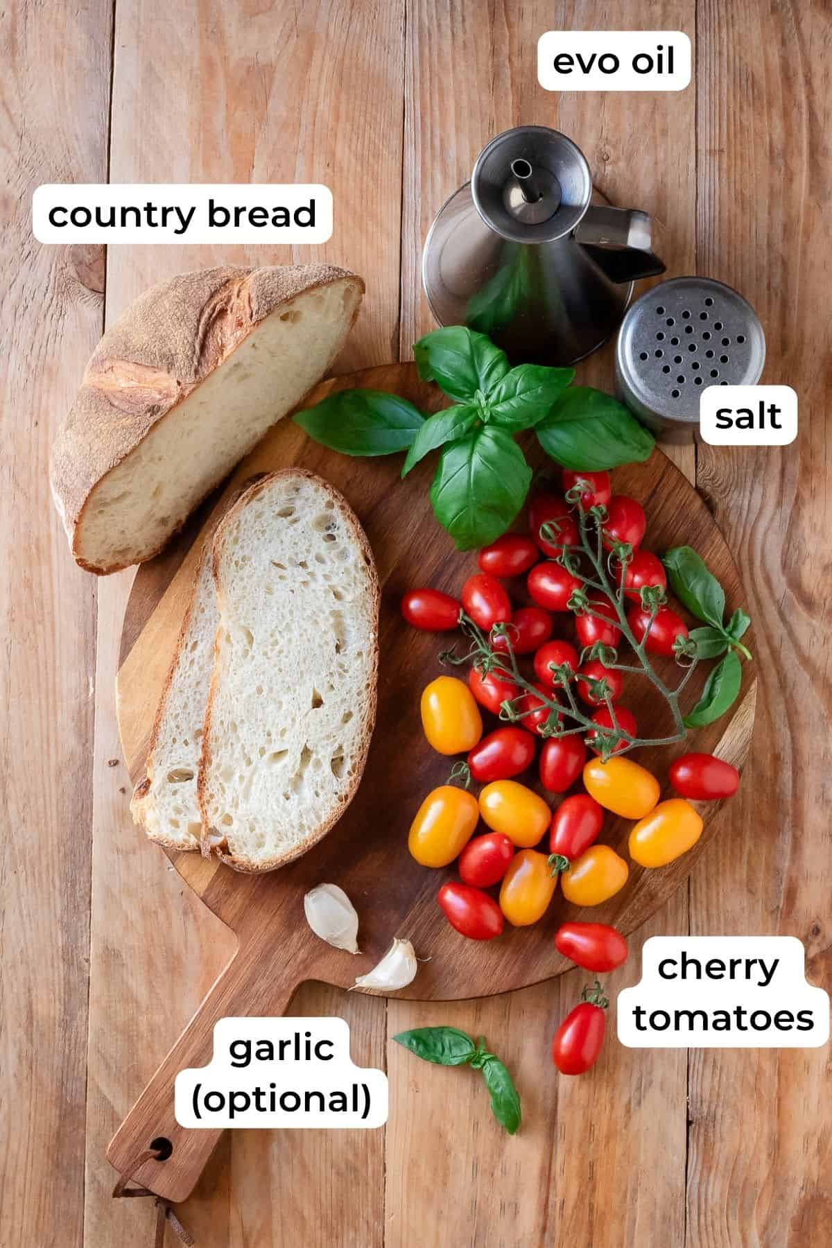 Ingredients needed to make cherry tomato bruschetta laid on a wooden surface.