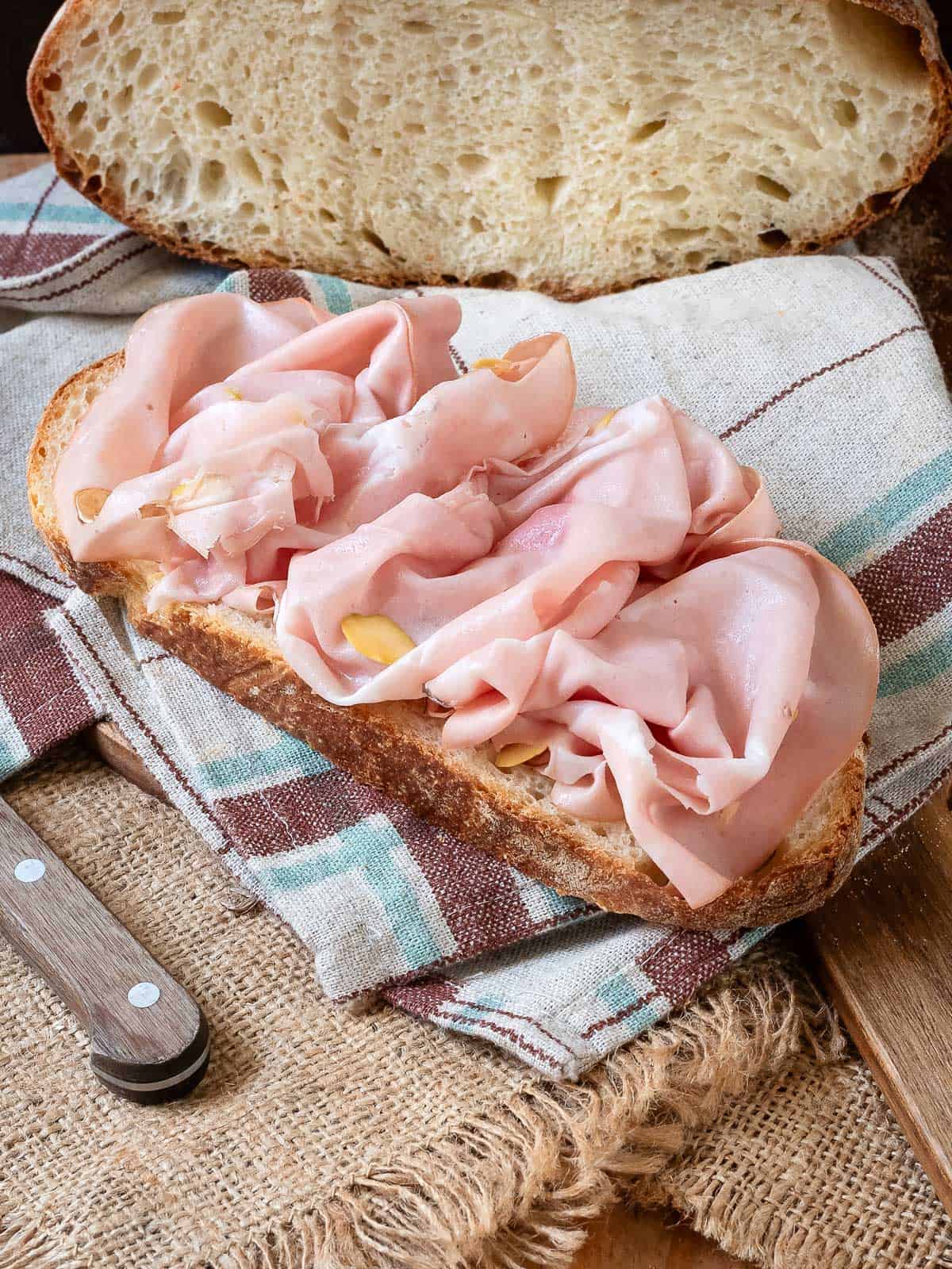 A slice of pugliese bread topped with thinly sliced Mortadella.