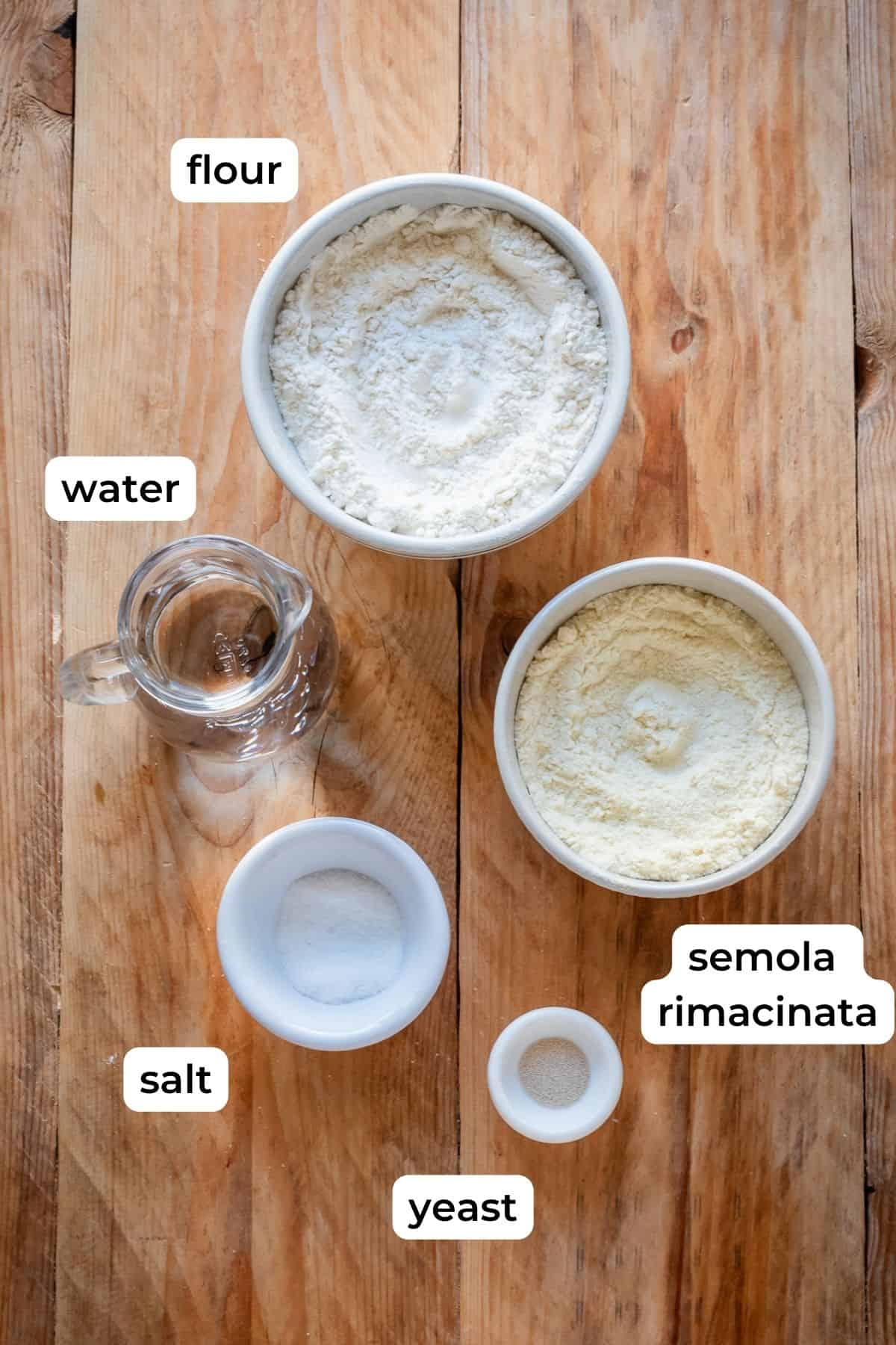 Ingredients needed for pugliese bread laid on a wooden surface.