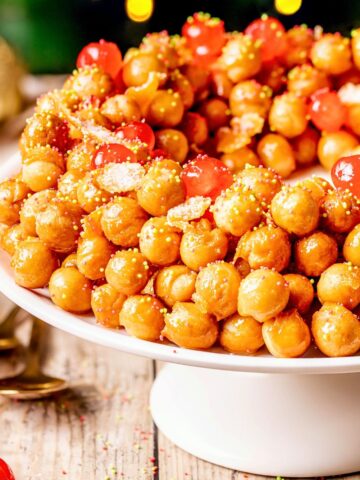 Struffoli honey balls on a white cake stand.