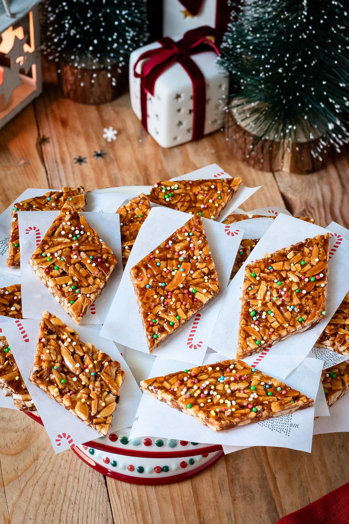 Almond brittle arranged on a dessert stand with Christmas decorations in the background.