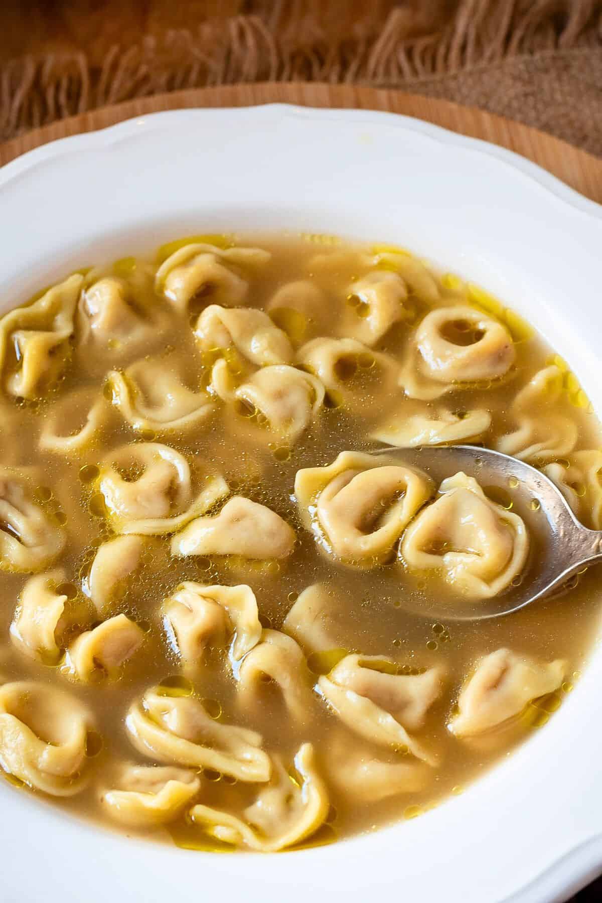 Scooping tortellini in brodo with a spoon.