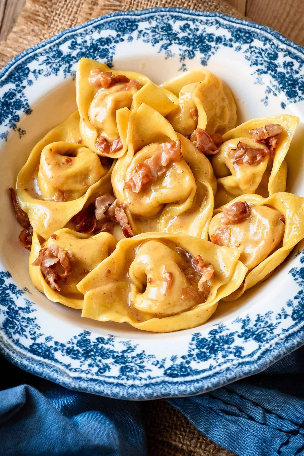 Cappellacci pasta prosciutto butter sauce on a plate with a blue rim.