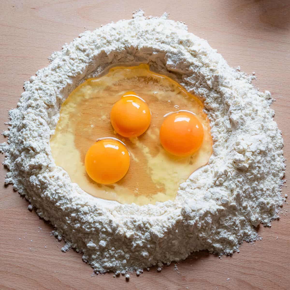 Eggs in a well of flour on a wooden surface.