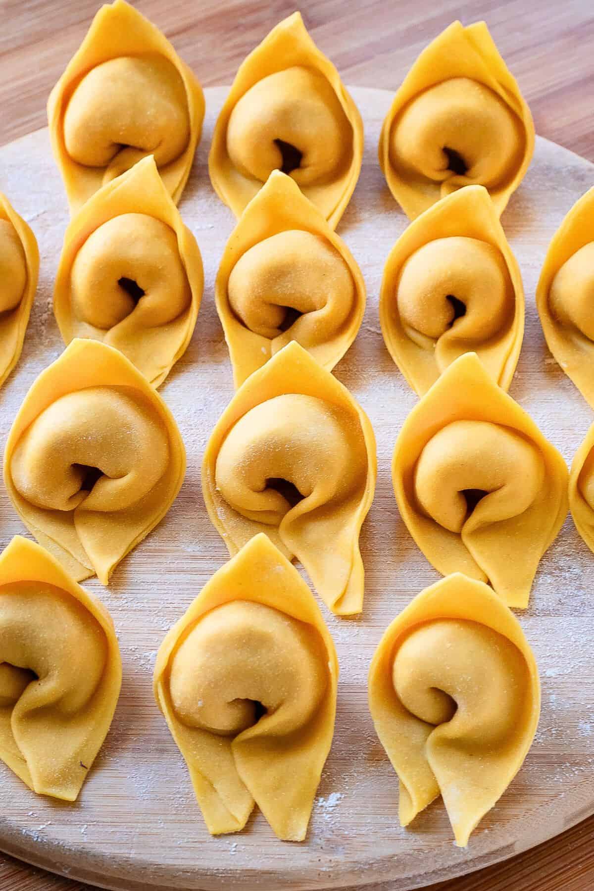 Freshly made cappellacci pasta lined on a wooden board.